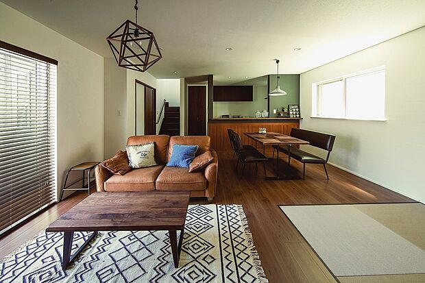 【【当社施工例】LDK】ブラウンのフローリングが温かみを感じさせる、落ち着いた内装のLDKです。腰高窓から明るい陽光が注ぎ込みます。グリーンのアクセントクロスがおしゃれなカウンターキッチンに映える空間です。