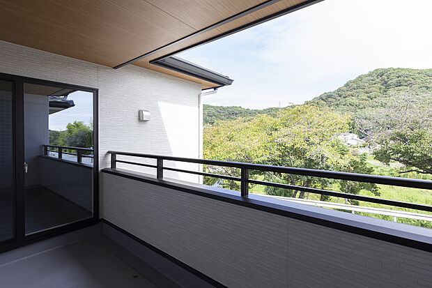 【【2階バルコニー/A号地】】木目の軒天があたたかみを添えるバルコニーは屋根付きで雨に濡れにくく、天気の良い日は手すりを使って布団もふかふかに。手すりの向こうには緑や青空が広がり、四季の移ろいが日常に感じられます。