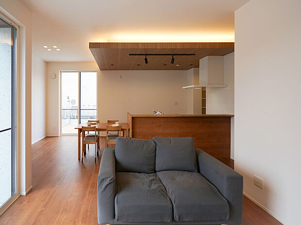 【A棟リビング】キッチン上部には木目の折下げ天井+間接照明が施され、空間のアクセントに。