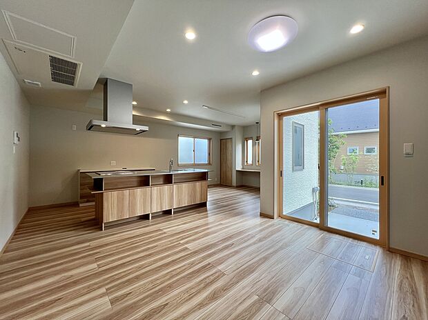 【【LDK/6号棟】】優しい色合いのフローリングが明るい雰囲気を演出する1階のLDKです。広さは約19.5帖で、リビング階段・アイランドキッチンを採用したコミュニケーションを育める空間。
