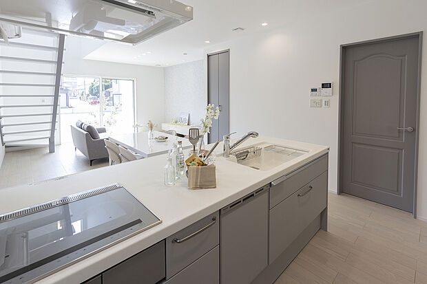 【1階キッチン/A号地モデルハウス】フラットキッチンや明るいトーンのフロアを設え、やわらかな印象のリビング空間。フラットキッチンは調理中にリビングのご家族との会話を楽しめ、食器の受け渡しもスムーズ。