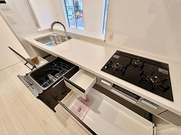 【キッチン】
コンロは三口仕様+グリル付き。ワークトップ下に、スライド式の収納が備わっています。対面部分はL字に開口しているため、リビング側まで見渡しやすそうです。