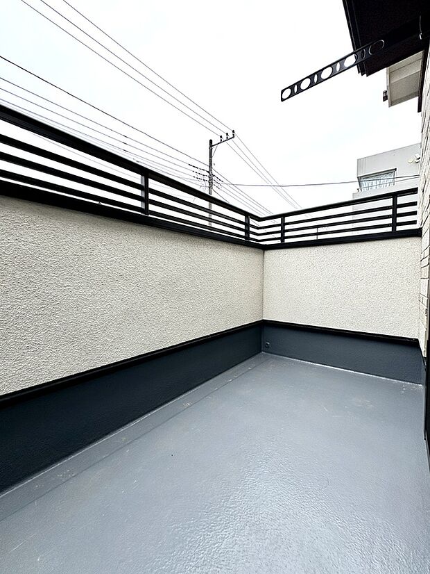 【【バルコニー/2号棟】】LDKから出入り可能な西向きのバルコニーです。物干しが設置されています。腰壁は、転落防止と道路からの視線を遮る役割を果たしています。