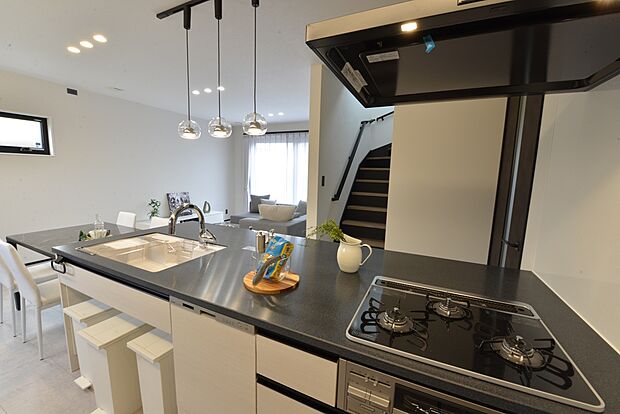 【【1階キッチン/B号地モデルハウス】】ワークトップは存在感を放つブラックの人造大理石カウンターに。グリル付き3口コンロや食器洗い乾燥機を搭載した、機能的なシステムキッチン。シンク下には分別用に複数のゴミ箱を設置できるスペースもございます。