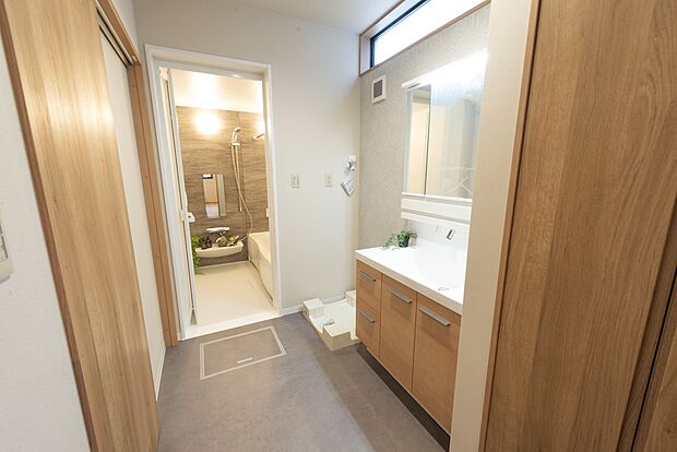 【【1階洗面脱衣室/E号地モデルハウス】】高い位置の窓からやわらかな光が注ぐウェットエリア。洗面化粧台横には収納を備え、リネンなどが収まります。シンク横の扉からだけでなく1階ホールからLDKに入らず出入りができ、帰宅時の手洗いも◎