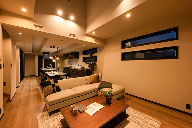 【A号棟：リビング】温かみのある照明と木の質感が調和するリビング。吹抜けの開放感と陰影が生み出す上質な空気に包まれ、家族の時間がゆったりと流れます。