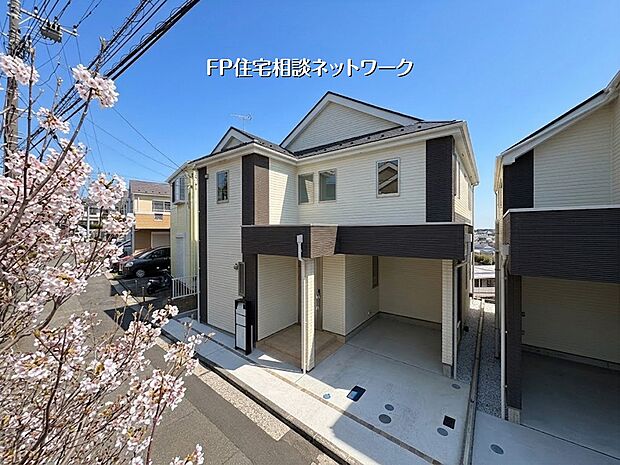 【外観】  明るい日差しと満開の桜が彩る、清潔感あふれる新築住宅。機能的なビルトインガレージを備え、並列駐車も可能です。開放的な住環境で、家族の新しい物語をここから始めませんか。