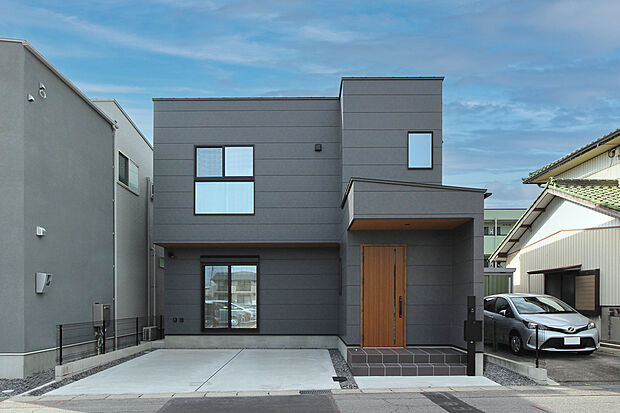 A棟｜シンプルなダークグレーのサイディングを基調に、玄関と軒天に木目を取り入れることで、温かみのあるアクセントをプラス。落ち着いた雰囲気と洗練されたデザインが魅力の外観です。