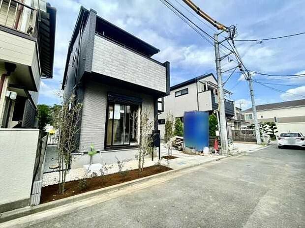 【前面道路含む現地写真】バルコニーと大開口窓の見える外観写真。南側のアスファルト舗装道路に面し、植栽と駐車1台分のスペースが確認できます。完成予定：2026年10月。