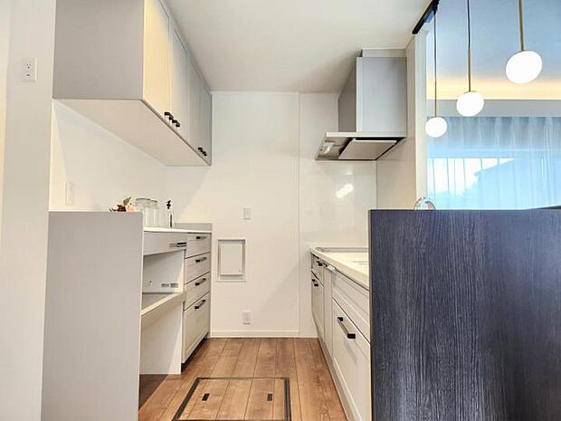 【【A区画キッチン】】気になる手元を隠せる対面スタイルのシステムキッチン。調理中の散らかりを気にせず作業できるうえ、水ハネなどを防ぎます。背面には家電収納もあり収納場所には困りません。（2024年7月撮影）