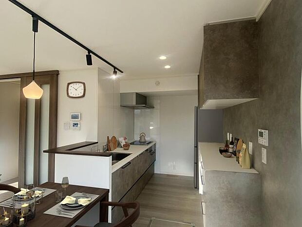 【D棟キッチン】モダンで機能的なキッチン。シンプルなデザインとダークカラーのキャビネットが特徴で、広々とした作業スペースと収納棚が備わっています。（2025年11月撮影）