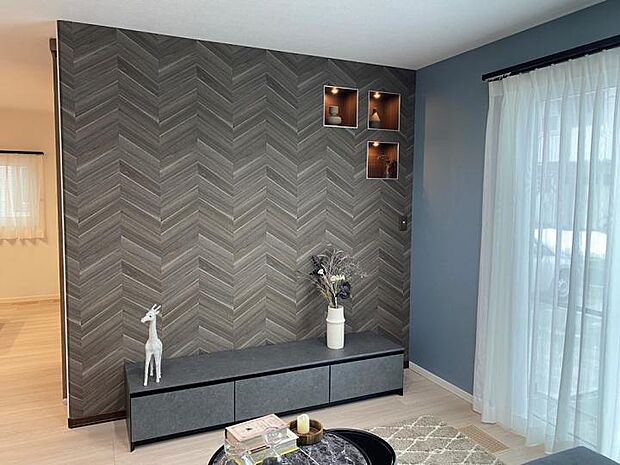 【A棟リビング(2025年1月撮影)】テレビボードの背面は、ブラックのヘリンボーン柄クロスに。思い出やコレクションなどを飾れるニッチもご用意しました。