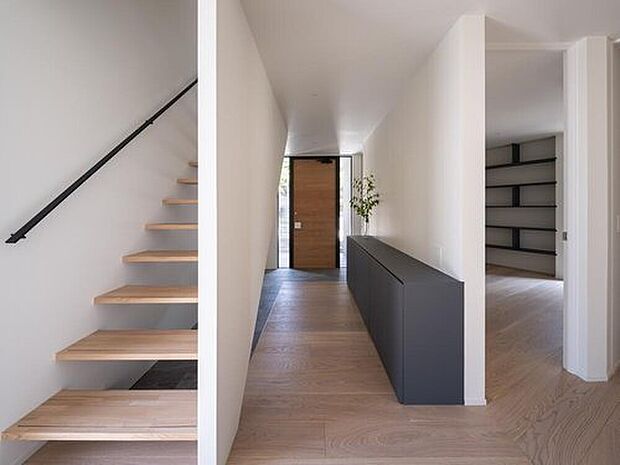 ミニマルで洗練された玄関ホールは、明るい木目のフローリング、浮いた階段、そしてモダンなグレージュの収納が、開放感と機能性を兼ね備えた上質な空間を演出しています。光の使い方も美しいです。