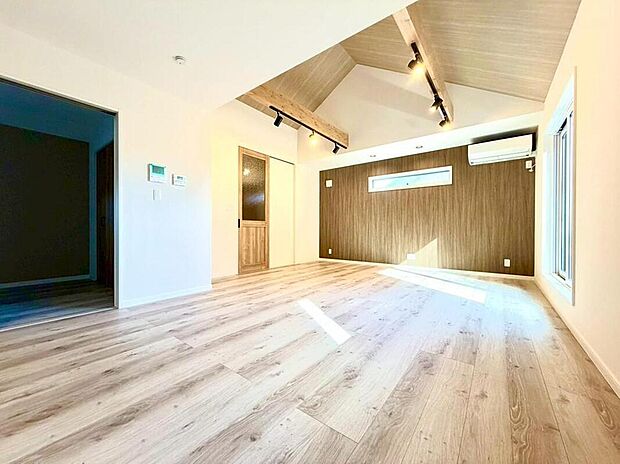 勾配天井と木目調のアクセントウォールが印象的なリビング。明るい陽光が降り注ぎ、家族の笑顔が自然と集まる、開放感あふれる空間です。