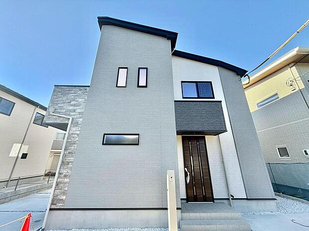 青空に映える、洗練されたデザインの戸建て。グレーと白のツートンカラーがモダンな印象を与え、家族の新しい暮らしを彩ります。明るい陽光が降り注ぐ、開放的な住まいです。