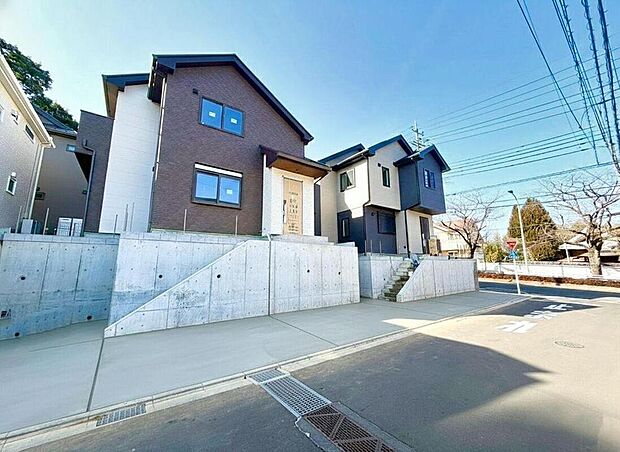 【現地外観写真】青空に映える、モダンで落ち着いた色合いの戸建てが並ぶ新築街並み。新しい暮らしが始まる予感に満ちた、家族の笑顔が溢れる住まいです。