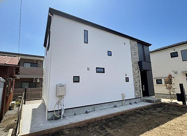 【【現地外観写真】】白と黒のコントラストが美しい、洗練された外観デザイン。広々とした駐車スペースは、家族の車をゆったり停められ、子育て世代にも嬉しい快適な毎日を叶えます。