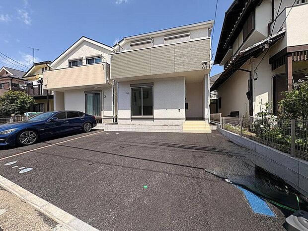 【現地外観写真】緑豊かな街並みに馴染む白の邸宅。並列2台のカースペースが暮らしにゆとりを与え、高度地区ならではの広い空が開放感を演出します。