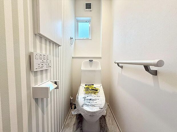 【トイレ】ストライプの壁紙が空間を明るく演出。手すり付きで立ち座りもスムーズ、小窓からの自然光がさらに清潔感を引き立てます。機能性とデザイン性を両立させた、家族みんなが毎日気持ちよく使える安心の空間です。