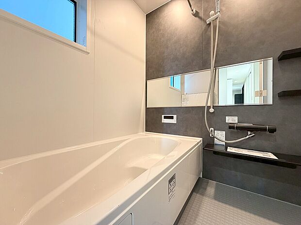 【浴室　D号棟現地写真】■リクシル　システムバスルーム「AX」。フロアはスポンジが奥まで入り掃除がラクラク。また独自の断熱層を使用しているため冬場でも冷やっとしません。