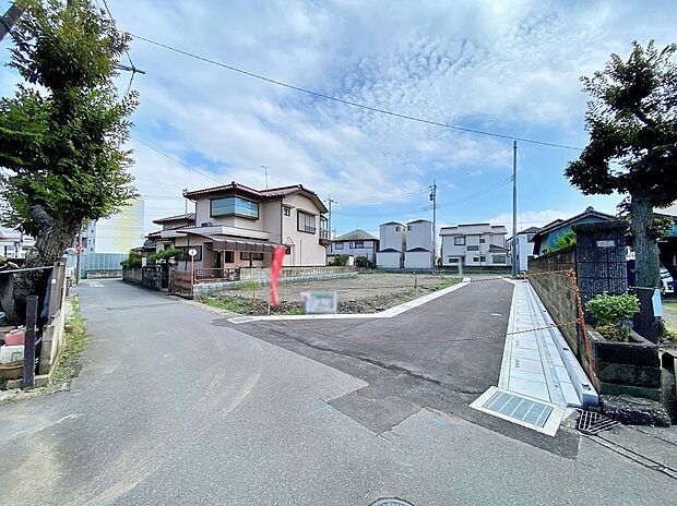 【前面道路含む現地写真】八潮市大曽根の分譲地で造成中の区画と作業車両、アスファルト舗装の前面道路が写っています。道路幅4～6m、駐車2台可、木造2階建予定（土地100m2台）。完成予定2026年11月。