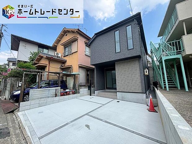【現地外観写真】ダークグレーの木造2階建て外観。コンクリート舗装の並列2台駐車スペースがあり、道路幅約6.3mに面しています。土地107.89m2・建物94.62m2。