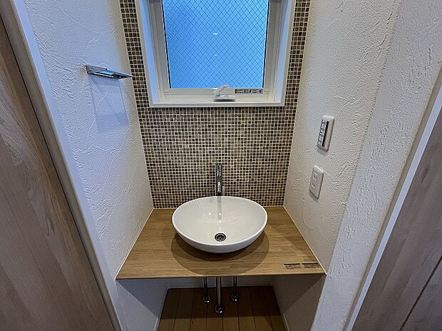 【１階 手洗いコーナー】メインの洗面室とは別に、玄関を入ってすぐのところにセカンド洗面台を設置。コロンとしたかわいらしい小型の洗面ボウルは、外から帰ってきてすぐに手洗いとうがいができるので、小スペースながら機能的！ウイルスはドアノブから感染につながることもあり、風邪や感染症などの予防になり、いつでも清潔な状態で室内へ。遊んで帰ってきた子供も自然と手洗いが習慣化され、来客時にはわざわざ洗面室を使って頂かなくて済みます。また、壁に施されたモザイクタイルは、遊び心が溢れるデザインでインテリアとしても楽しめると人気です。