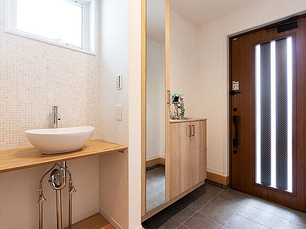 【-】メインの洗面室とは別に、玄関を入ってすぐのところにセカンド洗面台を設置。コロンとしたかわいらしい小型の洗面ボウルは、外から帰ってきてすぐに手洗いとうがいができるので、小スペースながら機能的！ウイルスはドアノブから感染につながることもあり、風邪や感染症などの予防になり、いつでも清潔な状態で室内へ。遊んで帰ってきた子供も自然と手洗いが習慣化され、来客時にはわざわざ洗面室を使って頂かなくて済みます。また、壁に施されたモザイクタイルは、遊び心が溢れるデザインでインテリアとしても楽しめると人気です。