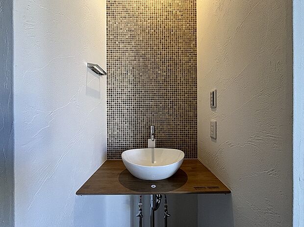 【１階手洗いコーナー　】メインの洗面室とは別に、玄関を入ってすぐのところにセカンド洗面台を設置。コロンとしたかわいらしい小型の洗面ボウルは、外から帰ってきてすぐに手洗いとうがいができるので、小スペースながら機能的！ウイルスはドアノブから感染につながることもあり、風邪や感染症などの予防になり、いつでも清潔な状態で室内へ。遊んで帰ってきた子供も自然と手洗いが習慣化され、来客時にはわざわざ洗面室を使って頂かなくて済みます。また、壁に施されたモザイクタイルは、遊び心が溢れるデザインでインテリアとしても楽しめると人気です。