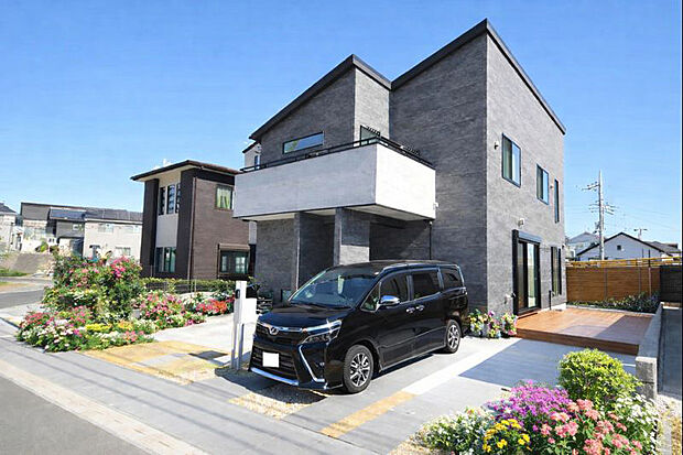 【外観(施工例)】重厚なグレー外壁と迫力のバルコニー、開放的なウッドデッキが魅力の邸宅。