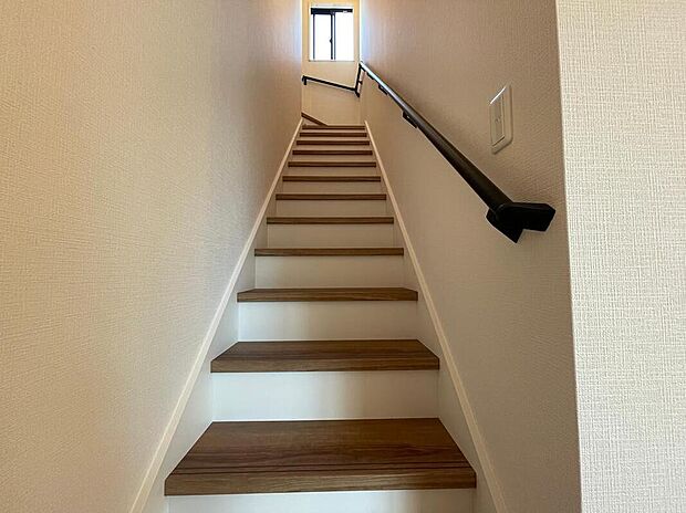 【【リビング階段】】家族の気配を感じられるリビング階段。
木目調の踏板と白い蹴込みが明るく清潔感を演出し、視認性の高い手すりで安心感も確保。
上部の窓から自然光が差し込む、開放的な設計です。