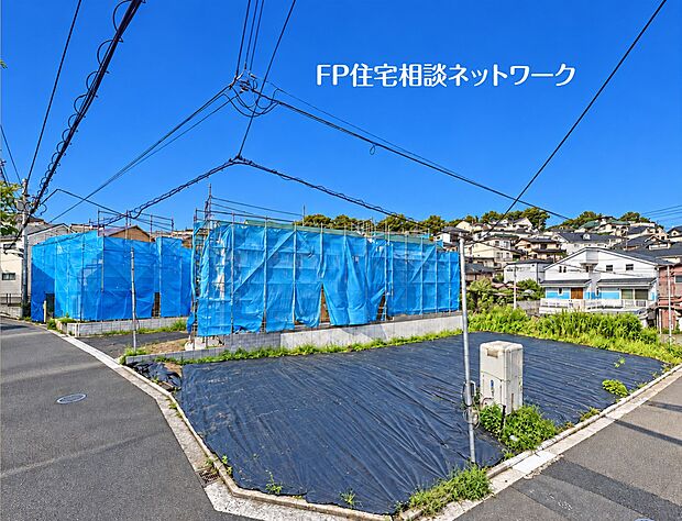 防草シートが敷かれ、現地の状況が確認しやすい角地の様子です。隣接する区画ではすでに建物の建築工事が進められており、周辺は新しい街並みが形成されつつある落ち着いた住宅街です。