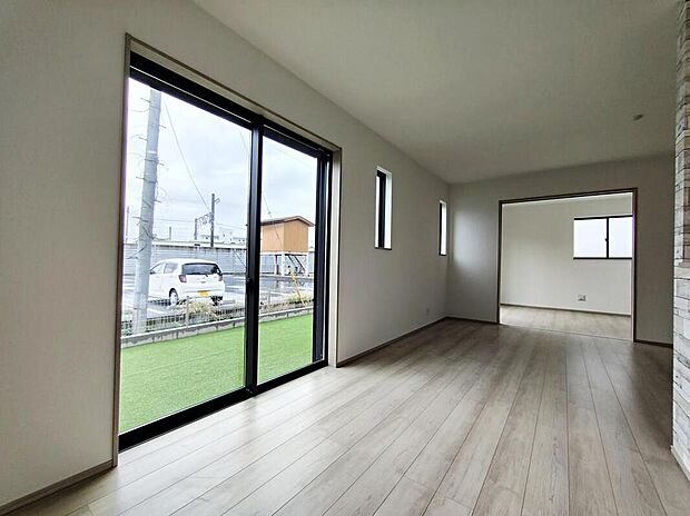 大きな掃き出し窓と高窓から明るい光が差し込み、広々とした床面が伸び、隣室への動線も良好で開放的な居心地を叶えます。木目床で温かみがあり、庭の緑が望めます。