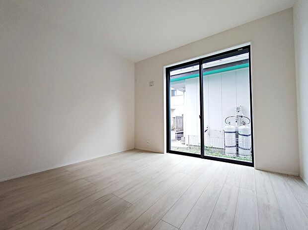 【居室】白い壁と明るいフローリングの室内。大きな掃き出し窓で採光が良く、外部スペースに面しています。