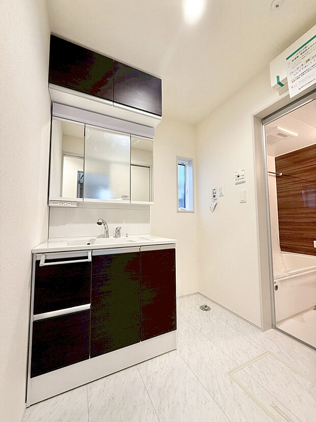【【洗面台 ｜ 1号棟】】三面鏡付きの洗面化粧台です。豊富な収納スペースが備わっており、ヘアドライヤーや化粧品などをすっきり収納できます。窓付きのため、湿気対策にも◎