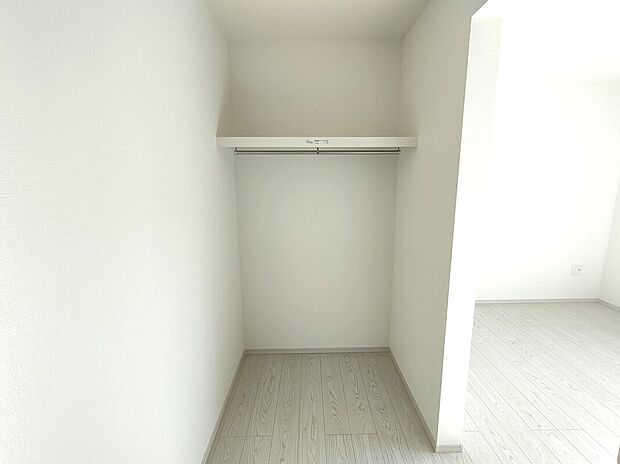 【ウォークインクローゼット】両側にハンガーパイプと棚を備えた、収納力の高い主寝室のウォークインクローゼット。白を基調とした内装と明るい床材が清潔感を演出し、衣類や小物をすっきり整理。暮らしにゆとりをもたらす機能的な収納空間です♪