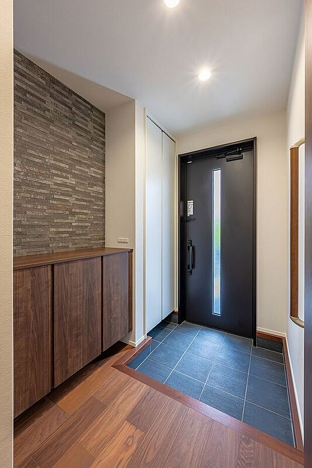 【玄関】■２号地玄関　濃いブラウンの木目調と濃いグレーの壁面が印象的な玄関。黒のドアには採光パネルを採用し、光を取り込みつつプライバシーを守り、明るく開放的な空間を演出します。
