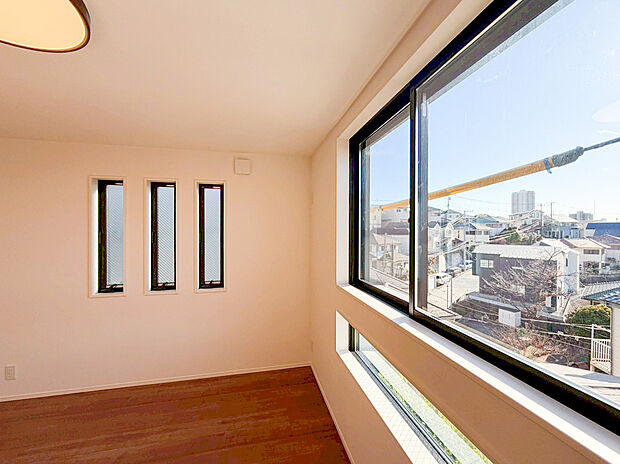 2面採光で明るさ抜群！開放感あふれる居室。大きなワイドサッシとデザイン性の高い縦長窓が、たっぷりの陽光と爽やかな風を取り込みます。暖色系のフローリングと白い壁が光を反射し、お部屋をより広々と演出。