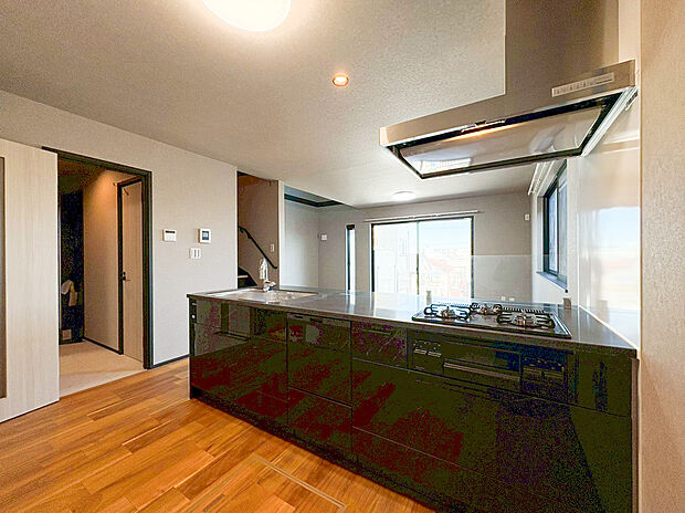 重厚感のあるダークトーンのパネルが映える、洗練されたフルオープンキッチンです。空間を遮る吊戸棚がないため、リビングの大きな窓から差し込む陽光を感じながら、開放的な気分でお料理を楽しめます。