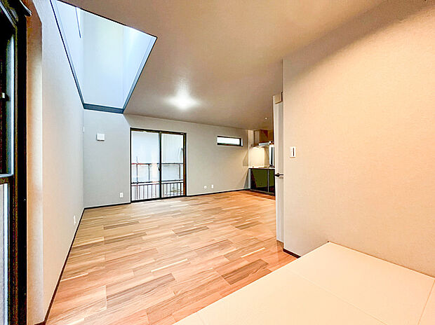 【リビング】リビングには、小上がりスペースが隣接。ここでは、畳の上でごろ寝をしたり、来客時には腰掛けたりと多様な使い方が可能です。奥のドアはバルコニーへ繋がり、採光窓とともに空間に広がりと明るさをもたらします。