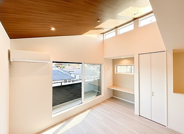 【リビング】天井が高く設計された勾配天井が、実際の帖数以上に開放感をもたらします 。上部の高窓からも光が降り注ぎ、一日中明るく心地よい空間です。