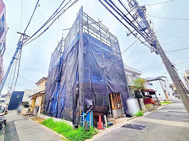 【現地外観写真】足場と養生ネットで覆われた建築中の外観写真。角地に面し前面道路は幅約3.2~4m、完成予定は2026年11月です。現地(2026年8月)撮影