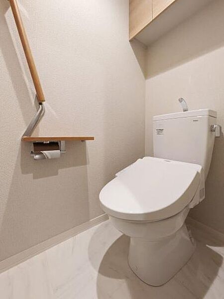 画像7:【トイレ】大理石調の床材とホワイトベースの色調で、高級感と清潔感を感じる内装のトイレ。手摺や棚、上部吊り戸を設置し、機能的に使いやすさを追求しました。