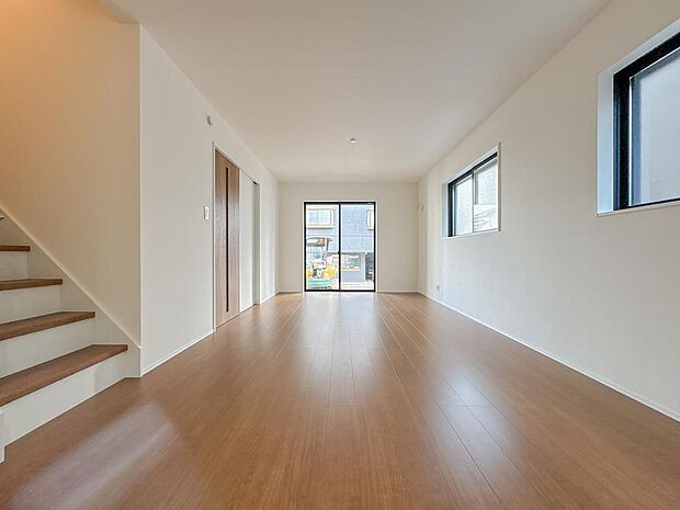 縦に広がる開放的なリビング空間。大きな窓から陽光が降り注ぎ、明るい家族の時間を育みます。白基調の壁とナチュラルな床材が調和。リビング階段が家族の繋がりを深めます。