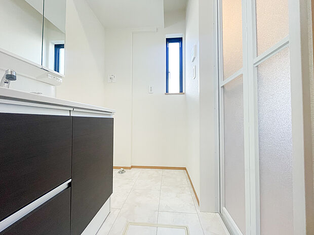 洗面台にはシックなダークブラウンのパネルが採用されており、白を基調とした空間に高級感のあるアクセントを加えています。