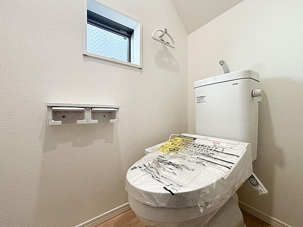 快適な温水洗浄便座付きトイレ。ペーパーホルダーは2連式で、上部の棚にはスマホや小物を置けて便利。頭上の収納スペースもしっかり確保されており、トイレットペーパーのストックや掃除用具もスッキリ片付きます。