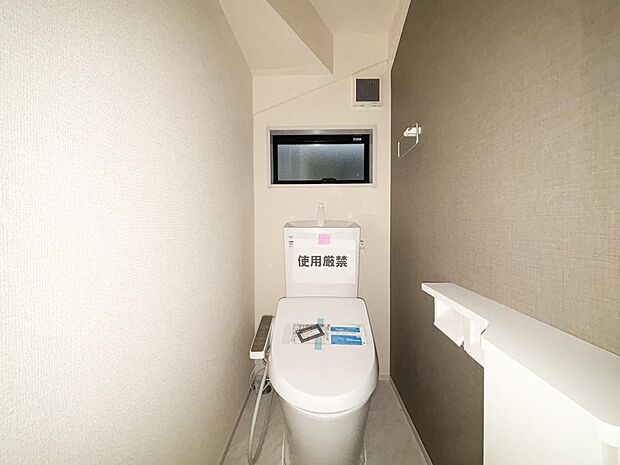 グレーの壁紙が落ち着いた雰囲気を演出するトイレ。温水洗浄便座や便利な棚付きで、毎日の生活に快適さをプラス。