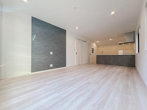 グレーのアセントクロスが映える、洗練されたLDK。開放的なオープンキッチンからはリビング全体が見渡せ、家族との会話も弾みます。白を基調とした明るい空間に、ダウンライトが上質な寛ぎを演出します。