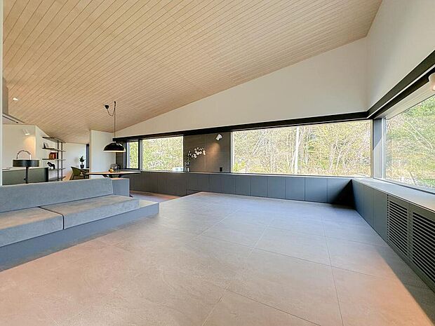 大開口の横長窓から緑を望む、開放感あふれるリビング空間。勾配天井と間接照明が上質な雰囲気を演出し、自然と家族が集まる心地よい暮らしを叶えます。