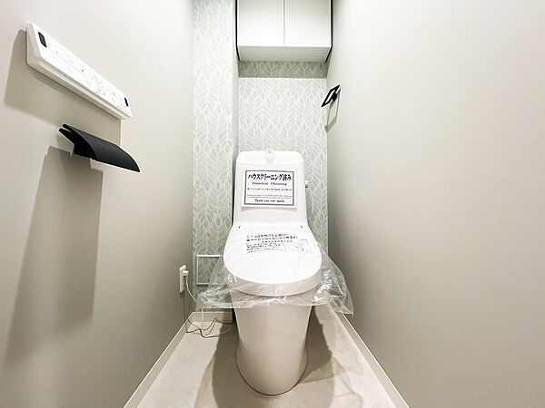 ボタニカル柄のアクセントクロスが爽やかで優しい雰囲気を演出するトイレ空間。毎日を快適に過ごせる温水洗浄便座を完備しています。上部にはトイレットペーパーのストック等に便利な吊戸棚付きです。